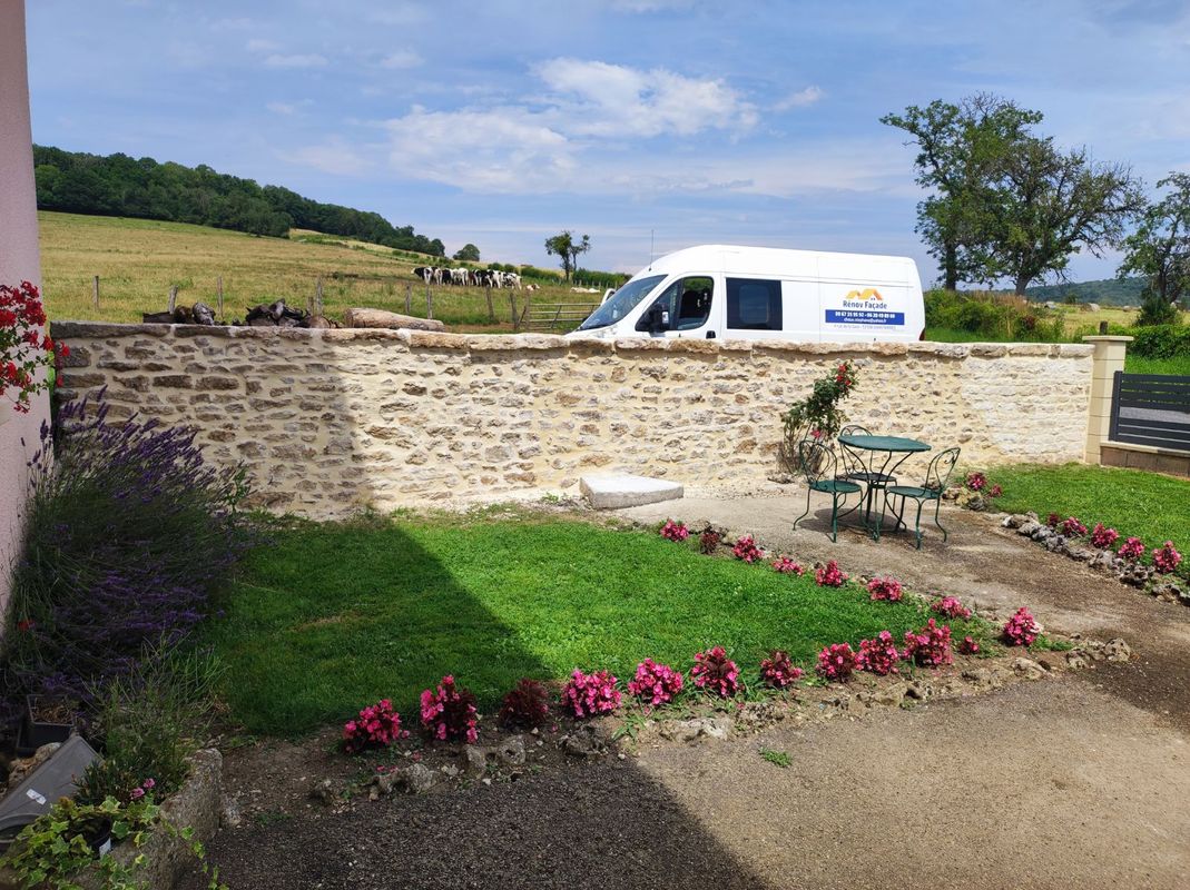 Mur en pierre restauré devant un pré, camion Rénov Façade